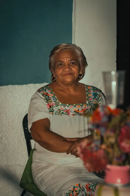 A smiling older woman seated comfortably in her own living room.