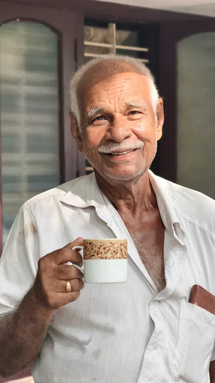 An older man smiling as he holds a warm cup of tea at home.