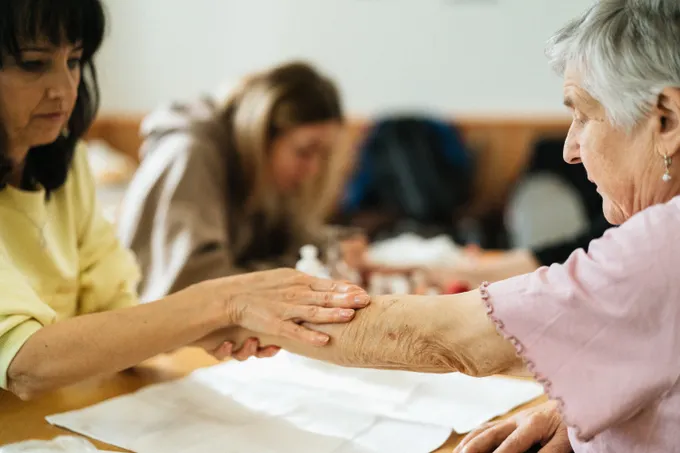 A caregiver and an older woman talking through care notes together at a table.