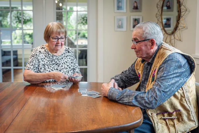 An older couple playing a game of cards together at their dining table at home.