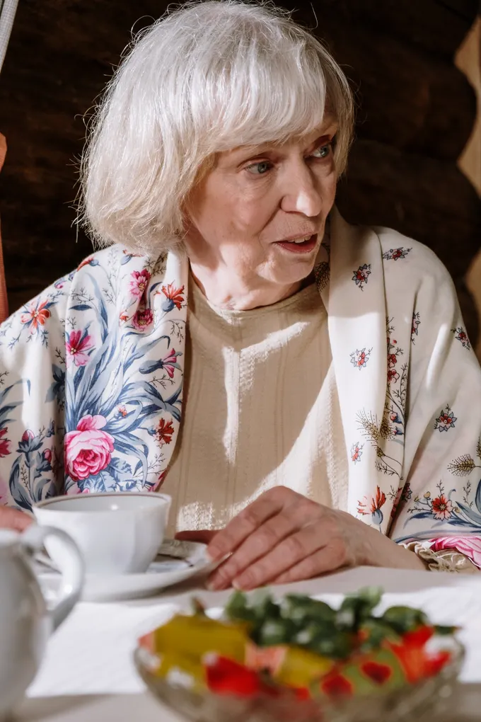 An older woman at her dining table with a freshly prepared meal in front of her.