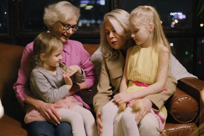 Two generations of a family sitting together on the sofa in a warm living room.